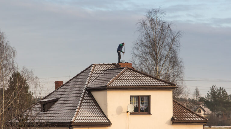 A chimney sweep cleans the chimney on the roof of a detached house in winter